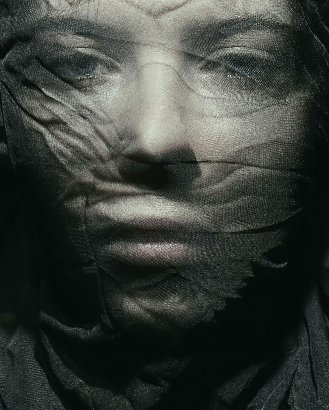 Editorial portrait of a woman behind dark sheer fabric