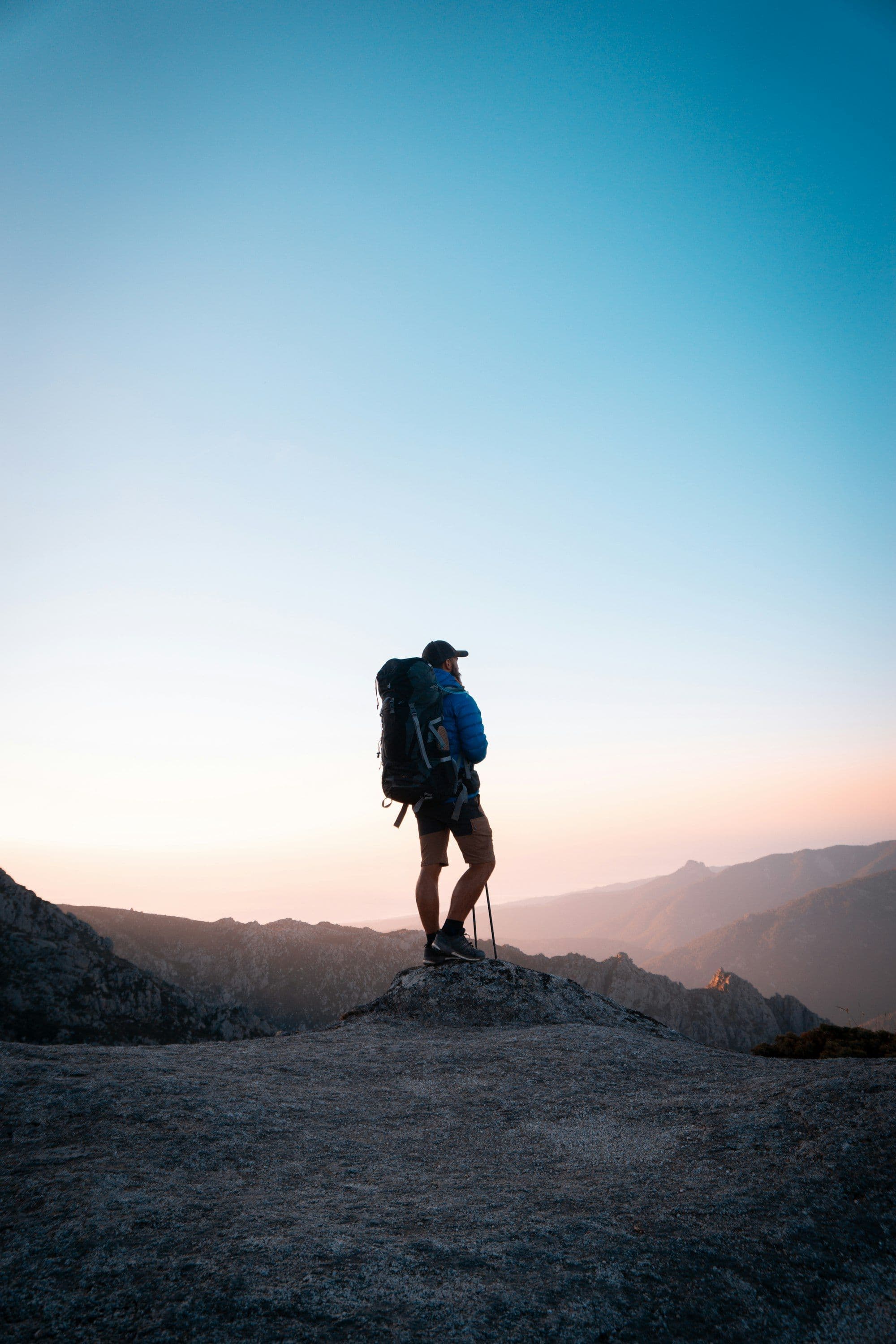 Photograph of a lone hiker on a mountain peak looking out at dawn