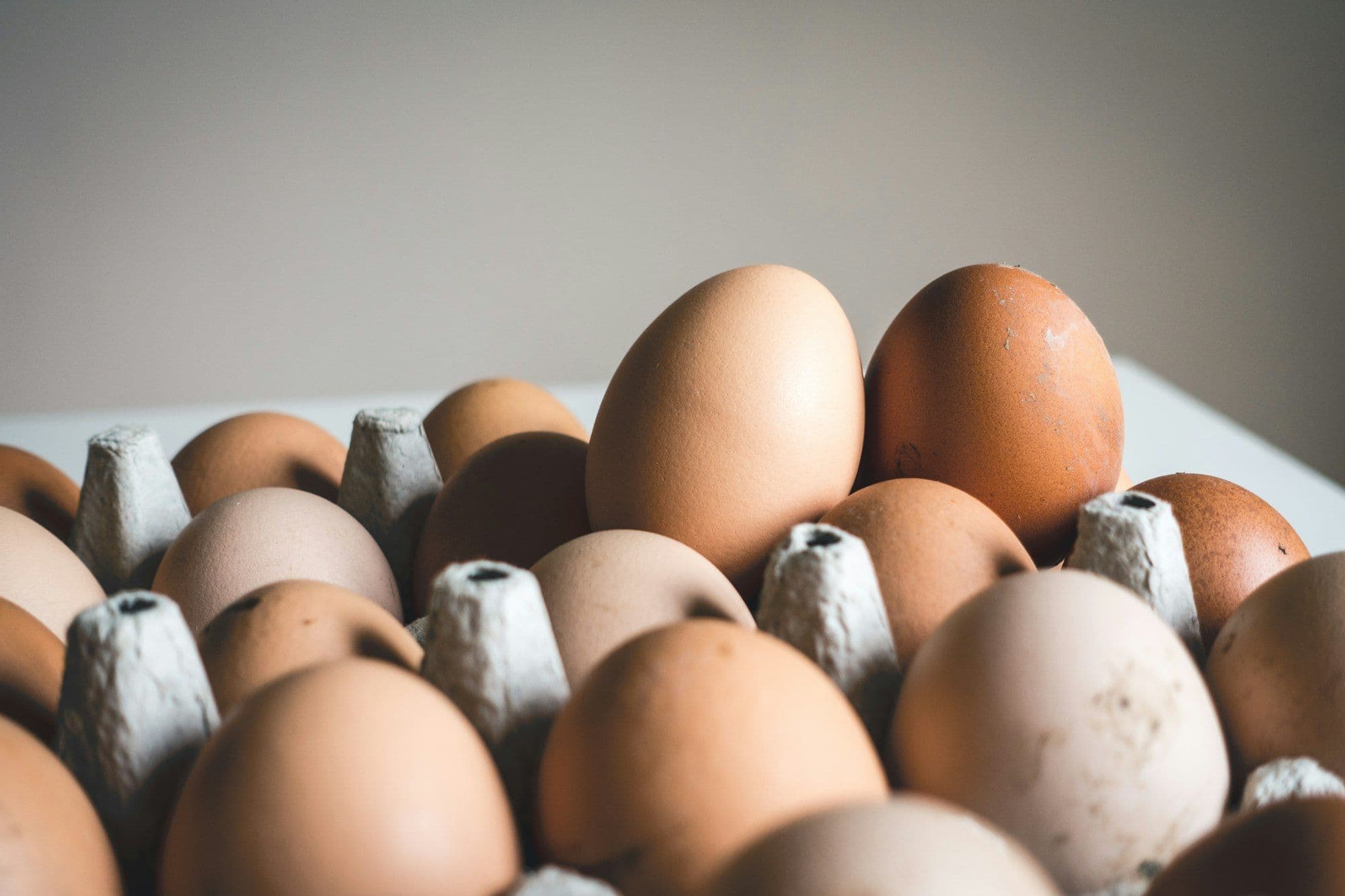 A tray of brown eggs in varying shades, two standing above the rest.